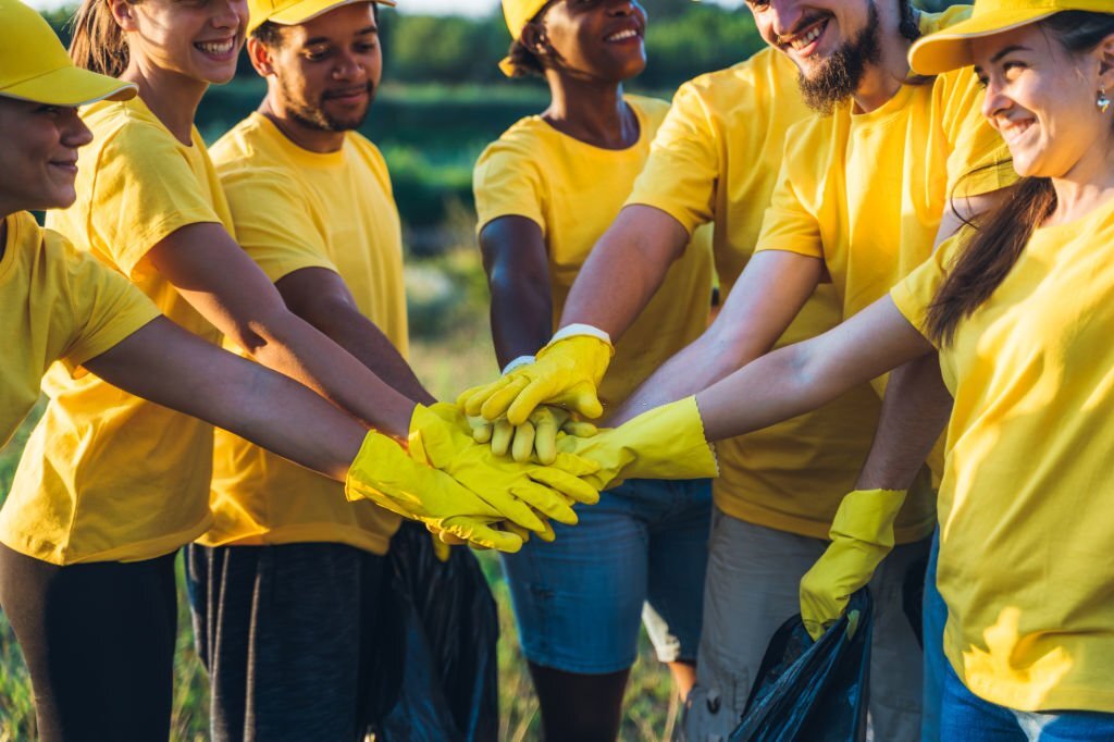 Young group of volunteers put hands together after collecting garbage in nature.